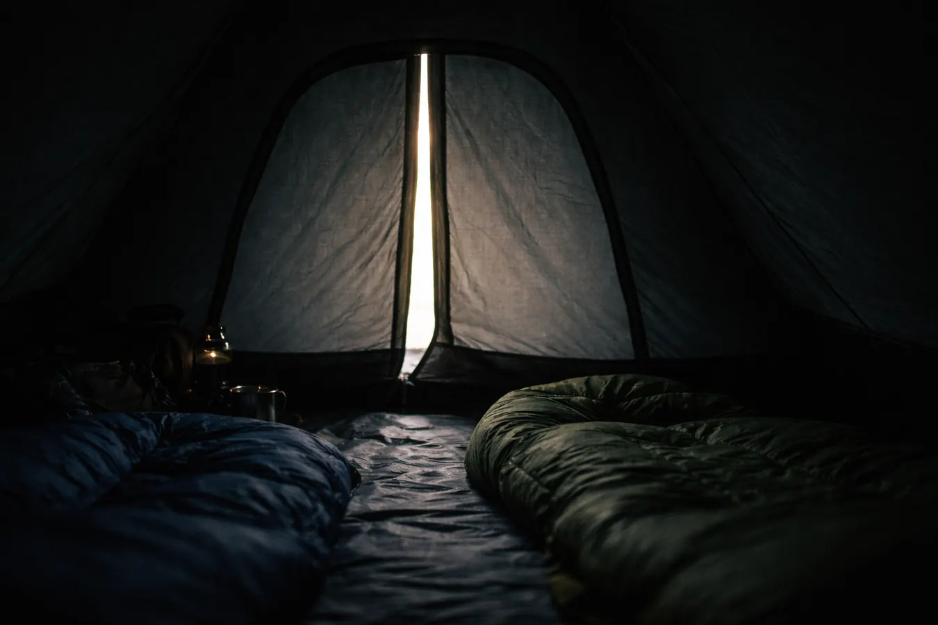 Interior of a dark tent showing near-blackout conditions with faint morning light edges around the door