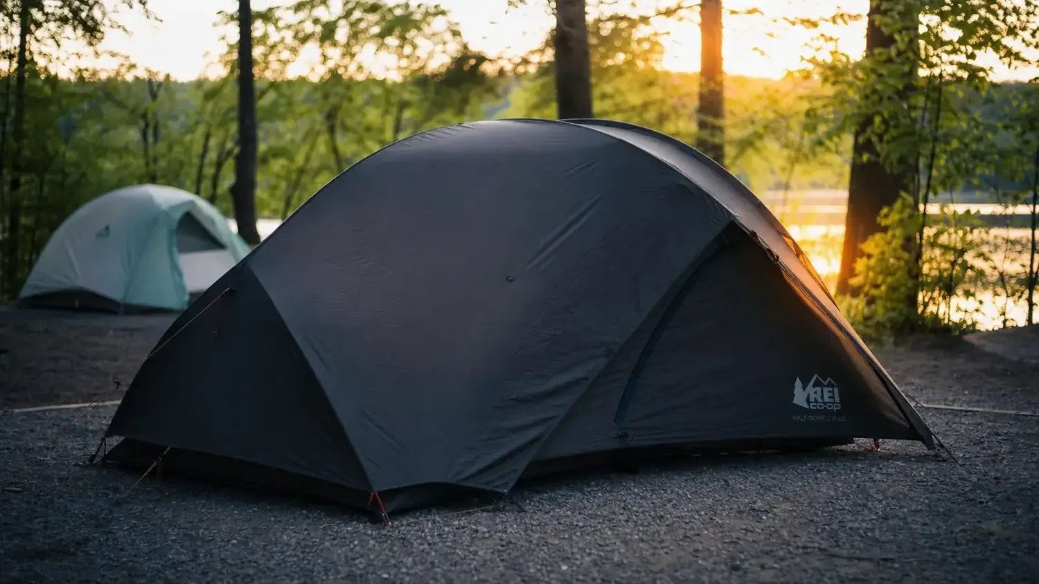 Coleman Sundome Dark Room 4-person tent pitched at a forested campsite at dusk, rain fly on, warm interior light visible through darkened fabric