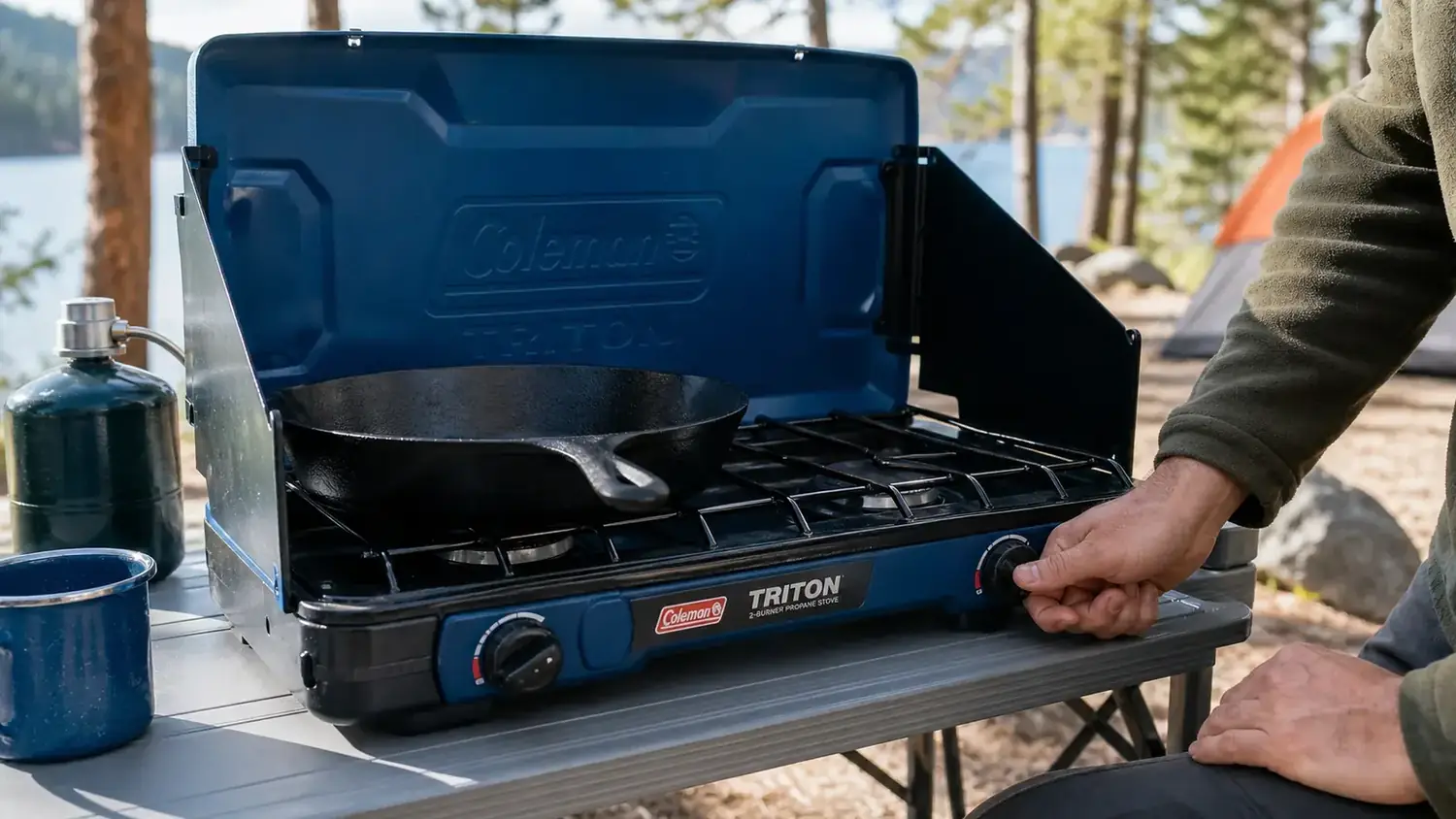 Hand adjusting the burner knob on a Coleman Triton stove with a cast-iron skillet on top