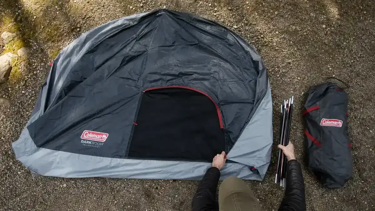 Overhead view of a tent footprint laid flat on cleared ground with poles and stakes laid out beside it