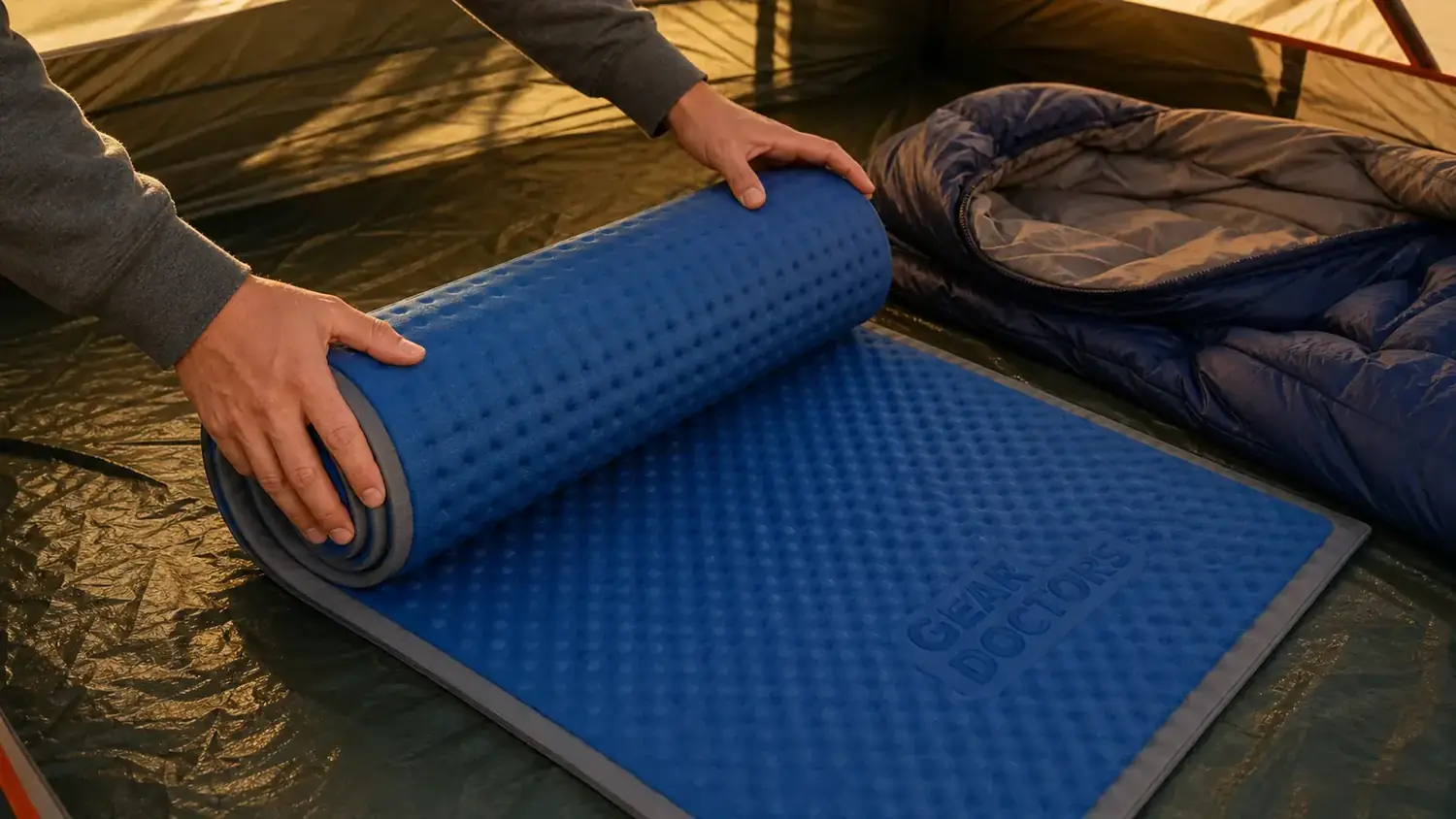 Person unrolling a self-inflating sleeping pad on tent floor next to a sleeping bag